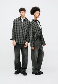 Fekete-fehér kockás ingek laza fazonban, laza sötétszürke farmerrel viselve. Mindkét szett nagy zsebekkel és hétköznapi fekete cipővel rendelkezik.