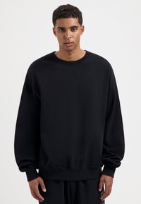 Zwarte sweatshirt met een relaxed fit, ronde halslijn en lange mouwen. Gemaakt van een gladde stof, voorzien van ribbelmanchetten en onderrand.