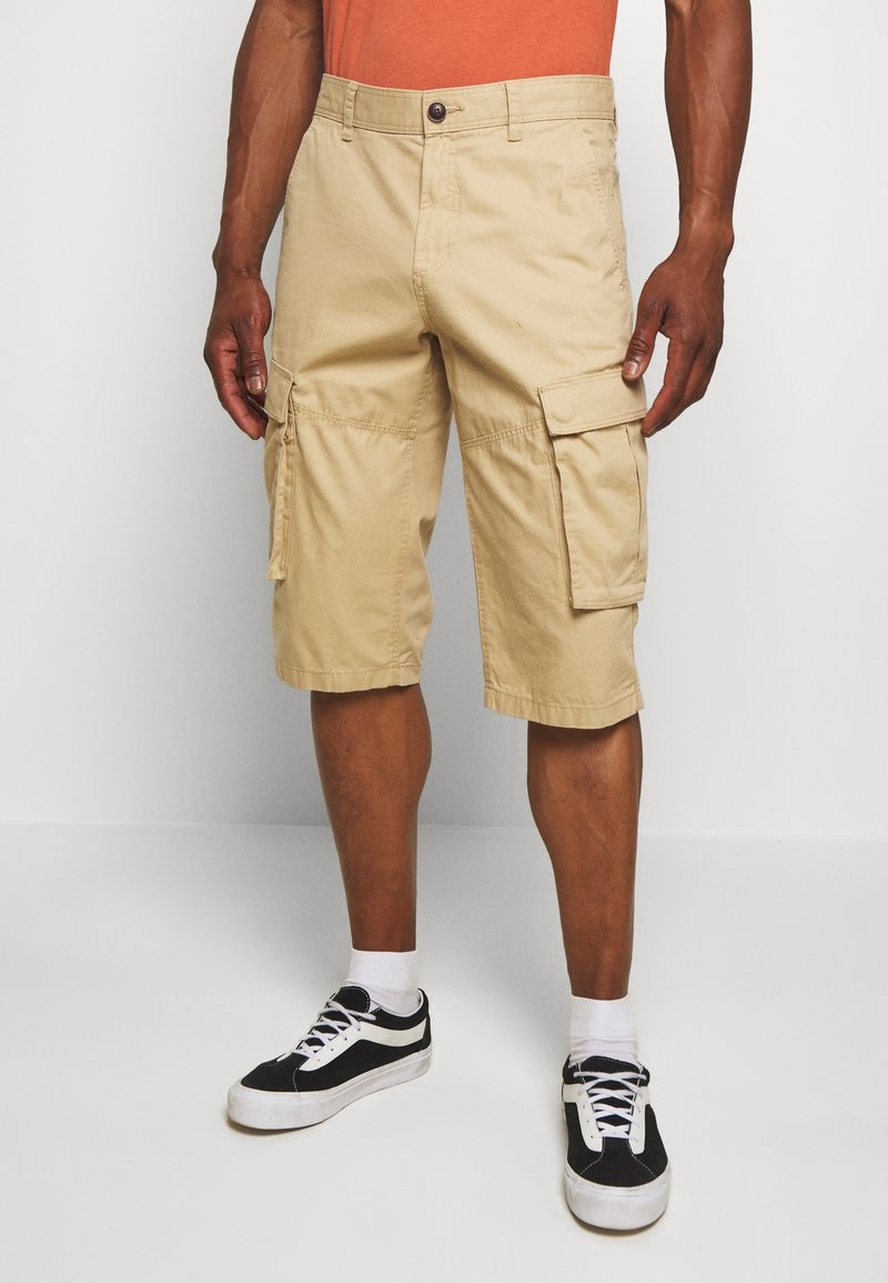 Shorts cargo kaki avec plusieurs poches latérales, une fermeture à boutons et une coupe droite. Assortis à des baskets noires et blanches.