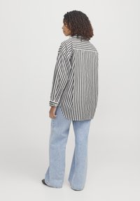 Sort og hvid stribet oversized skjorte med buet kant og knapmanchetter, parret med lyseblå flared jeans. Teksturen fremstår glat.