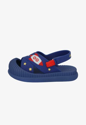 Sandalias azules con un diseño de cohete, correa roja y estrellas amarillas. Hechas de goma, con una suela texturizada y lados abiertos para ventilación.