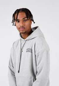 Szary sweatshirt z przednią kieszenią, sznurkiem do regulacji i nadrukowanym napisem "WRONG FRIENDS". Wykonany z miękkiego materiału, posiada luźny krój i kaptur.