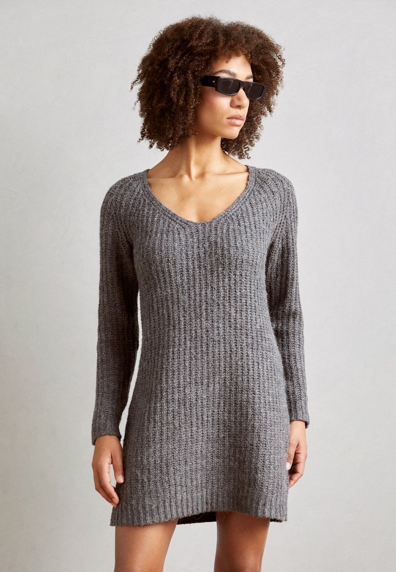Vestido de suéter gris de punto con un patrón acanalado texturizado, escote en V y mangas largas, que presenta un corte holgado y un dobladillo de longitud media.