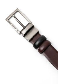 Brązowy skórzany pasek z szczotkowaną metalową klamrą, z wygrawerowanym logo. Na pasku splatają się dwa czarne skórzane akcenty.