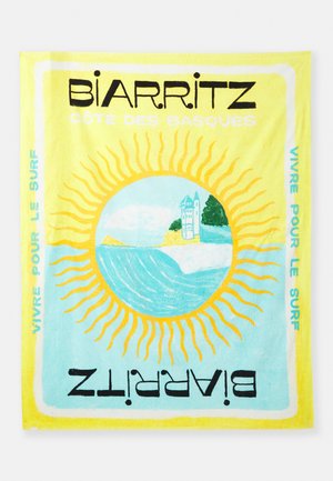 Puuvillane randarätik, millel on kollane ja sinine päikesemuster, koos julge musta ja türkiissinise tekstiga "BIARRITZ" ja "VIVRE POUR LE SURF".