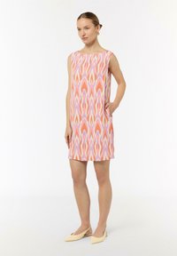 Ärmelloses Kleid in Rosa mit einem mehrfarbigen abstrakten Muster. Verfügt über seitliche Taschen und einen geraden Schnitt. Getragen mit beigen spitzen Ballerinas.