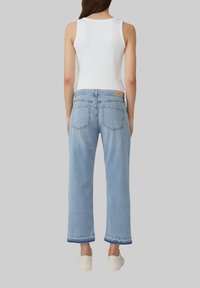 Hellblaue Jeans im weiten Schnitt, mit hoher Taille, fünf Taschen und fransigem Saum. Kombiniert mit einem weißen Tanktop.