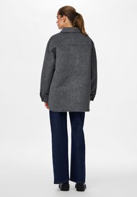 Γκρί oversized σακάκι από μαλλί με γιακά, με ευθεία γραμμή, χαλαρούς ώμους και λεπτομέρεια από πίσω με ραφή. Συνδυασμένο με σκούρες μπλε παντελόνες με φαρδιά πόδια.