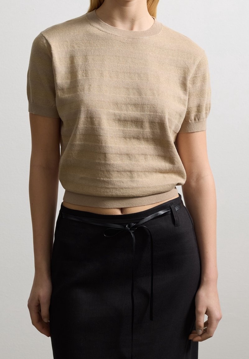 Beige gebreide trui met korte mouwen en een geribbelde halslijn en zoom, met een subtiele streepjespatroon. Gekleed met een zwarte rok die in de taille is gestrikt.