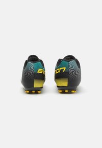 Botas de fútbol negras y verdes azules con un acento amarillo en degradé, presentando superficies texturizadas y tacos amarillos. "EVOLUCIÓN" impreso en amarillo.
