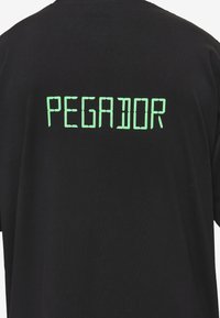 Sort t-shirt med grøn tekst "PEGADOR" på ryggen, med en glat overflade og korte ærmer.