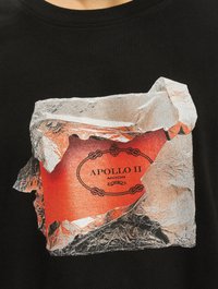 Sort bomulds-T-shirt med et grafisk design af krøllet sølvfolie, der afslører en orange baggrund med teksten "APOLLO II MOON" i dekorativ skrift.