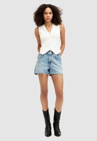Vit ribbad ärmlös topp med v-ringning och detalj med knappar, tillsammans med ljusblå denimshorts med fransade kanter och svarta ankelkängor.