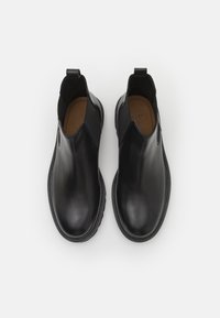 Mustad nahast chelsea saapad elastsete külgpanelidega ja silmuslingiga, millel on sile tekstuur ja ümar nina, valge tausta vastu.