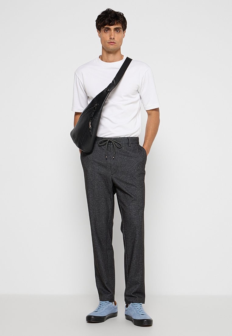 Grau gemusterte Hose mit Kordelzug, weißes kurzärmeliges Hemd und schwarze Umhängetasche. Hellblaue Sneakers runden den Look ab.