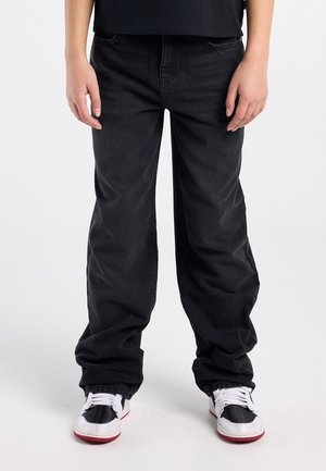 Zwarte denim jeans met een ontspannen pasvorm, voorzien van een klassiek ontwerp met vijf zakken en een subtiele textuur. Gecombineerd met witte en rode sneakers.