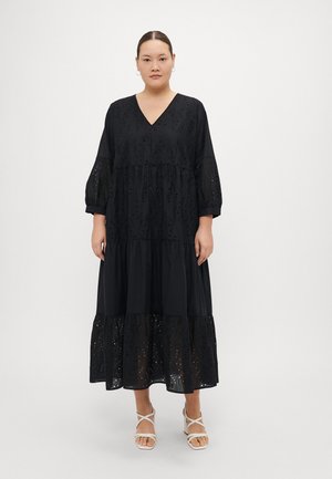 Zwarte, gelaagde maxidress met V-hals, kantversiering en geborduurde patronen. Driekwartmouwen en lichtgewicht stof. Draagt met sandaaltjes met bandjes.