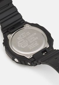 Montre en résine noire au design robuste, dotée d'un dos en acier inoxydable gravé de détails et fixée par des boulons, ainsi qu'un bracelet texturé.