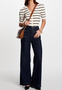 Højtaljede brede jeans i mørk denim, parret med en kortærmet stribet top i creme og sort, samt en brun skuldertaske.