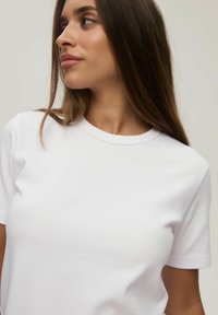 Biała bawełniana koszulka z krótkim rękawem i okrągłym dekoltem. Gładka tekstura, minimalistyczny design i dopasowany krój.