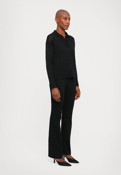 Black long-sleeve polo with button placket and textured shoulder accents, paired with black flared pants and pointed black heels.