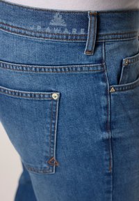 Jeans de denim azul con un corte ajustado, costuras naranjas, dos bolsillos traseros y un acento en forma de triángulo en el bolsillo derecho.