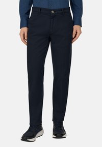 Granatowe spodnie wykonane z lekkiego materiału, wyposażone w zapięcie na guzik, szlufki na pasek i dopasowany krój. W zestawie z czarno-szarymi trampkami.