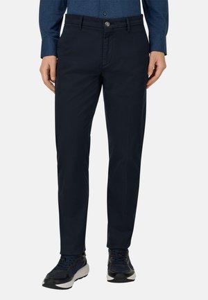 Navy siniset housut, jotka on valmistettu kevyestä kankaasta, varustettu nappisulkimella, vyölenkeillä ja slim fit -muotoilulla. Yhdistetty mustiin ja harmaisiin lenkkareihin.