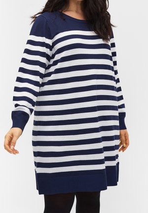 Kvinde iført en lang sweaterkjole med horisontale navy- og hvide striber, lange ærmer og ribbet kant.