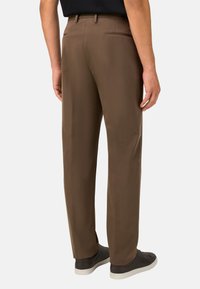 Rudos pritaikyti kelnės, pagamintos iš lygaus audinio, su tiesaus kirpimo dizainu, gale esančiomis kišenėmis ir vilkimos su tamsiais batais.