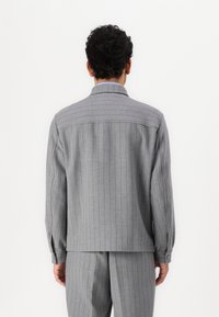 Grå rutig blazer med långa ärmar och knäppte manschetter. Mjuk tyg med vertikala ränder, som har en strukturerad krage och ryggåka.