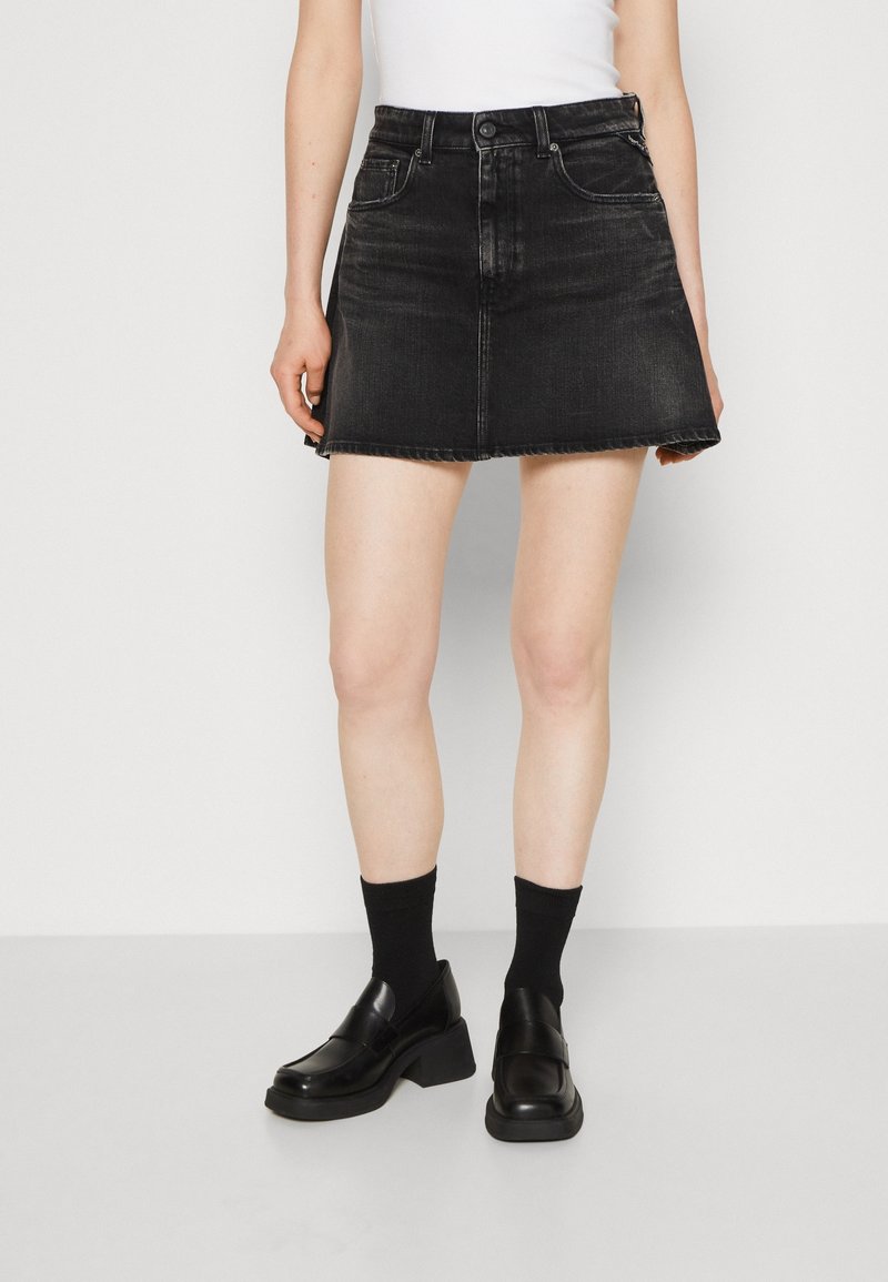 Černá džínová sukně s rozšířeným střihem, pěti kapsami a neupraveným lemem. Kombinováno s černými mokasínami a černými ponožkami délky ke kotníkům.