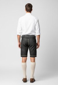 Men's black leather shorts with yellow piping, paired with knee-length beige socks and brown shoes, viewed from the back.