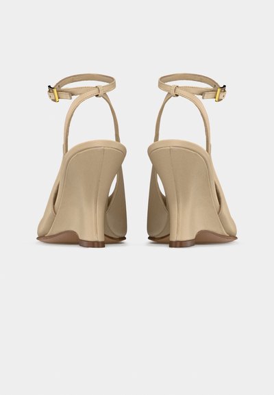 Μπεζ πλατφόρμες με λουράκια στον αστράγαλο και χρυσούς αγκράφες, εμφανιζόμενες από πίσω σε λευκό φόντο.