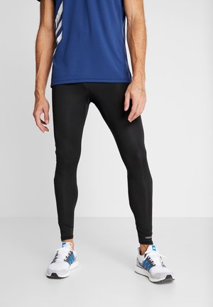 Leggings de sport noirs avec une coupe slim, présentant une texture lisse et un design minimaliste. Portés avec un t-shirt de sport bleu et des baskets blanches.