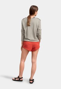 Felpa grigia chiara con maniche lunghe, abbinata a pantaloni corti rossi con orlo leggermente curvato. Sandali neri completano l'outfit.