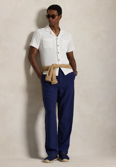 Λευκό, κοντομάνικο μπλουζάκι με υφή και δύο τσέπες στο στήθος, με κουμπιά, σε συνδυασμό με ναυτικό μπλε παντελόνι φαρδιάς γραμμής. Μπεζ πλεκτό δένεται στη μέση, casual υποδήματα.