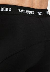 Cintura masculina que lleva puestos unos bóxers de la marca Smilodox de color negro, con costuras visibles y piel por encima de la cinturilla.