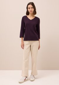 Maglietta a maniche lunghe viola scuro con scollatura a V abbinata a pantaloni beige chiaro a gamba larga e sneakers bianche. Texture liscia, design casual.