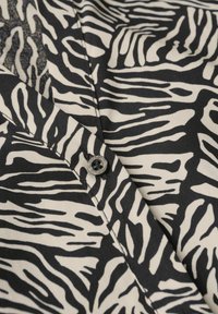 Camicetta bianca e nera con motivo a strisce zebra, realizzata in tessuto morbido. Un solo bottone è visibile al colletto.