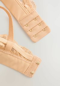 Cinghietto del reggiseno beige con bordo in pizzo, chiusura regolabile a gancio e asola con finiture dorate e texture del tessuto liscia.