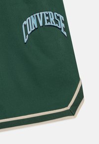 Zielone szorty z tkaniny węzełkowej, z jasnoniebieskim logo "CONVERSE", kontrastowymi beżowymi wykończeniami i luźnym krojem.