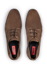 Chaussures à lacets en suede marron avec une texture lisse, bout arrondi et semelles en caoutchouc noires. Elles présentent des lacets marron et des accents de logo rouges à l'intérieur.