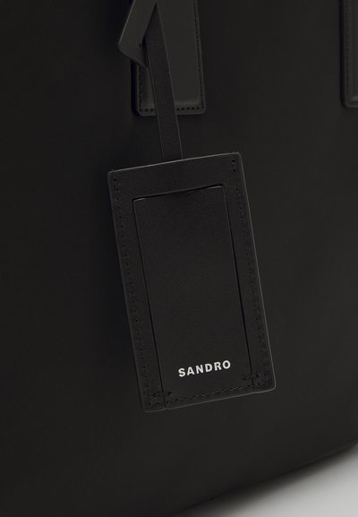 Sort lædertaske med et rektangulært mærke, præget med "SANDRO." Glat tekstur med minimalistisk design og rene syningdetaljer.