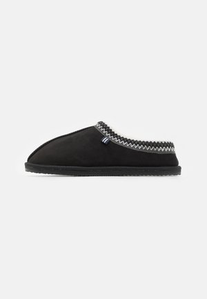 Black suede slipper with a round toe, white fleece lining, and decorative zigzag stitching around the collar. Flat rubber sole.