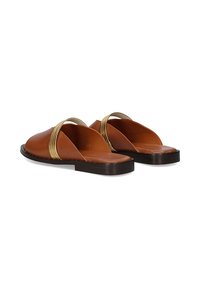 Sandalias de cuero marrón sin hebillas con una textura suave, diseño de corte flexible y correas con acentos dorados, colocadas sobre una suela plana oscura.