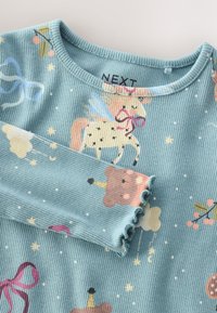 Türkiz színű bordázott hosszú ujjú ing állatmintákkal, többek között medvékkel és unikornisokkal, fodros mandzsettákkal és kerek nyakkivágással.