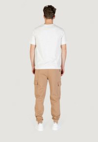 T-shirt grigio chiaro a maniche corte con taglio dritto, abbinato a pantaloni cargo beige con tasche laterali e polsini elastici, indossato con sneaker bianche.