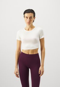 Hvite, ribbestrikkede, cropped t-skjorte kombinert med høyt liv, mørkelilla leggings. Glatt tekstur, tettsittende design, rund hals.