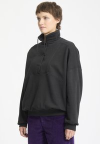 Maglione a pullover nero con alto collo, patta con bottoni e polsini a costine. Materiale spesso con vestibilità rilassata e sottili dettagli di cucitura.